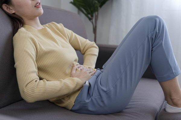 A woman lying on a couch holding her stomach, appearing to experience stomachache.